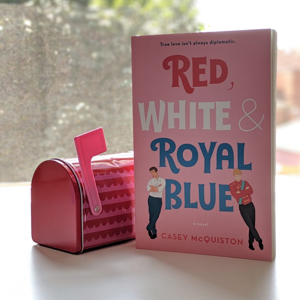 Red White and Royal Blue by Casey McQuiston next to a mini mailbox on a desk